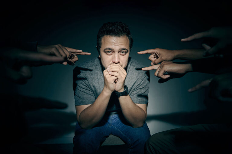 Man stressed out while being surrounded by people pointing at him (Getty Images/PeopleImages)