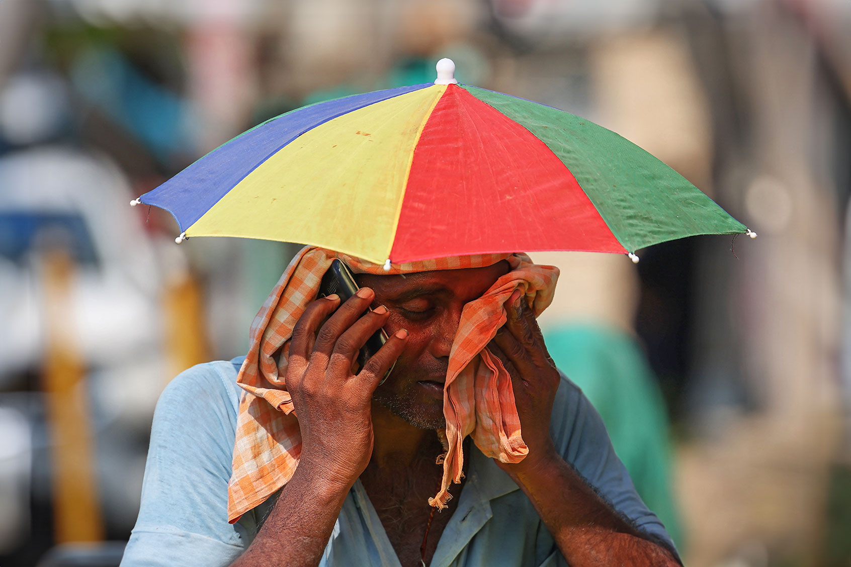 A vendor with an umbrella over his head talks on mobile phone as he wipes his face with a cloth on a hot summer day in Varanasi on May 27, 2024. (NIHARIKA KULKARNI/AFP via Getty Images)
