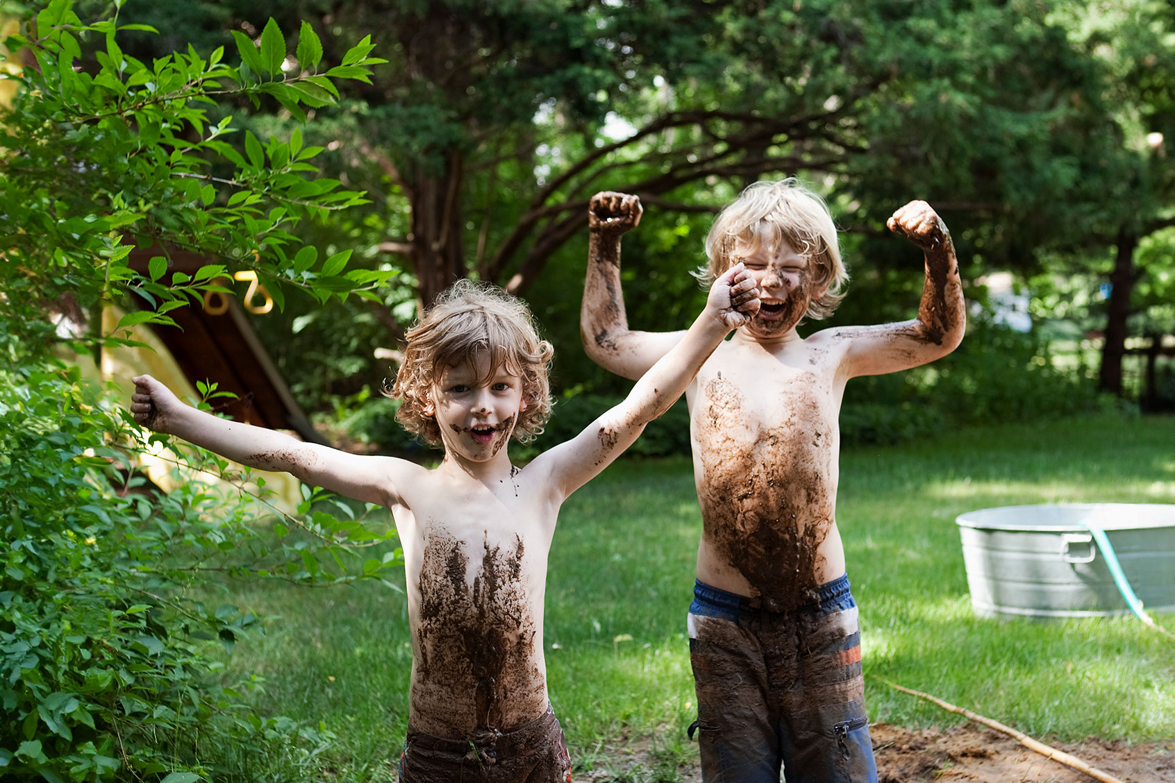 Two little boys covered in mud standing in a mud hole and laughing. (Getty Images/Andreas Kuehn)