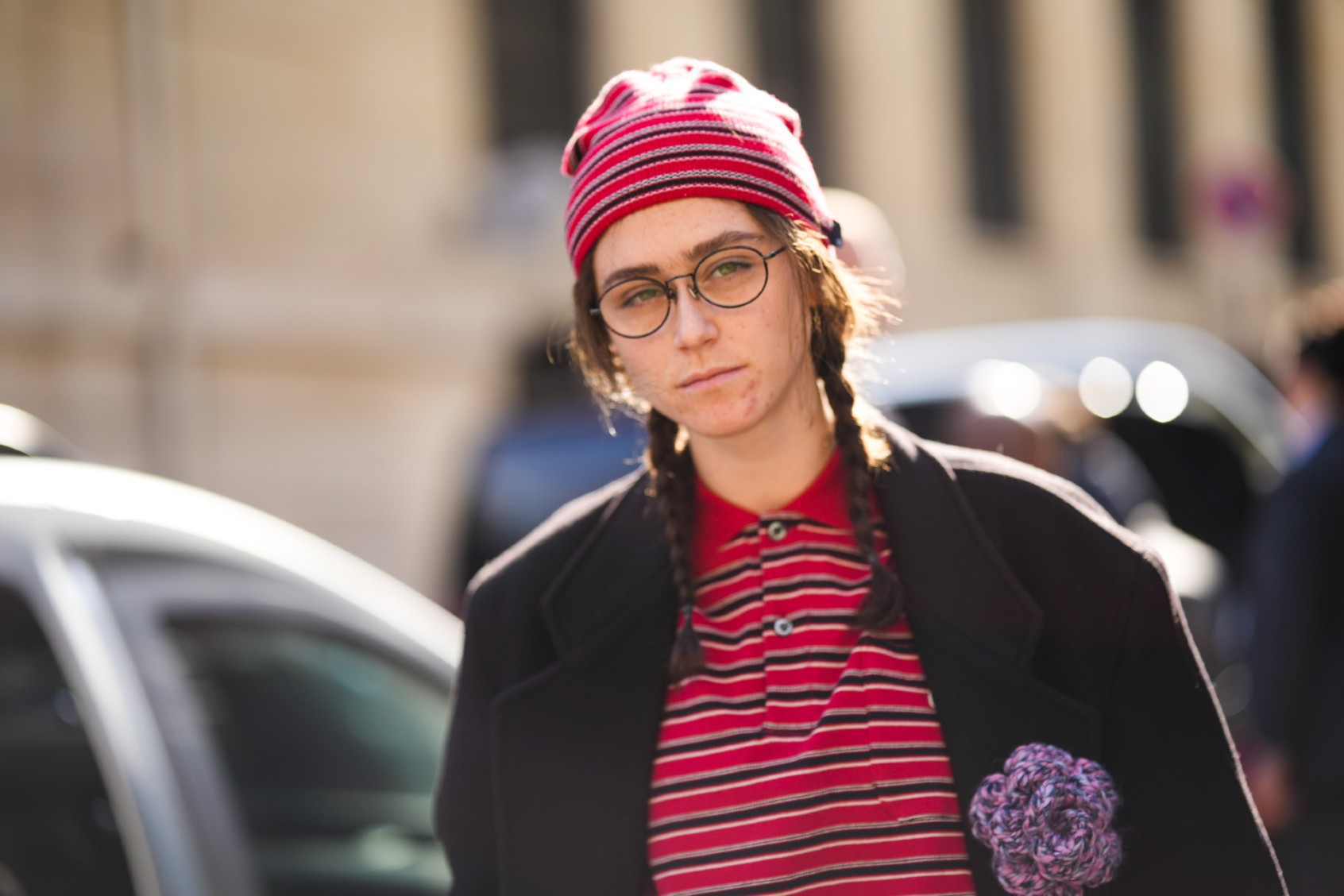 Ella Emhoff wears a red with black and white striped print pattern beanie, a matching red with black and white striped print pattern polo shirt, a black long coat with a purple flower brooch, black glasses, gray large pants, outside Dries Van Noten, during Paris Fashion Week - Womenswear Fall Winter 2023 2024, on March 01, 2023 in Paris, France. (Edward Berthelot/Getty Images)
