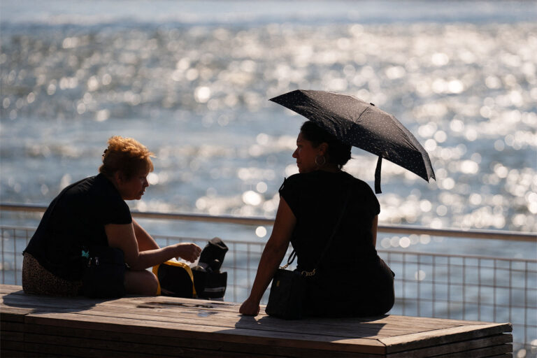 A person shields themself from the sun with an umbrella as people visit Domino Park in Brooklyn, New York, as a heat wave hits the northeast US on June 18, 2024. (ADAM GRAY/AFP via Getty Images)