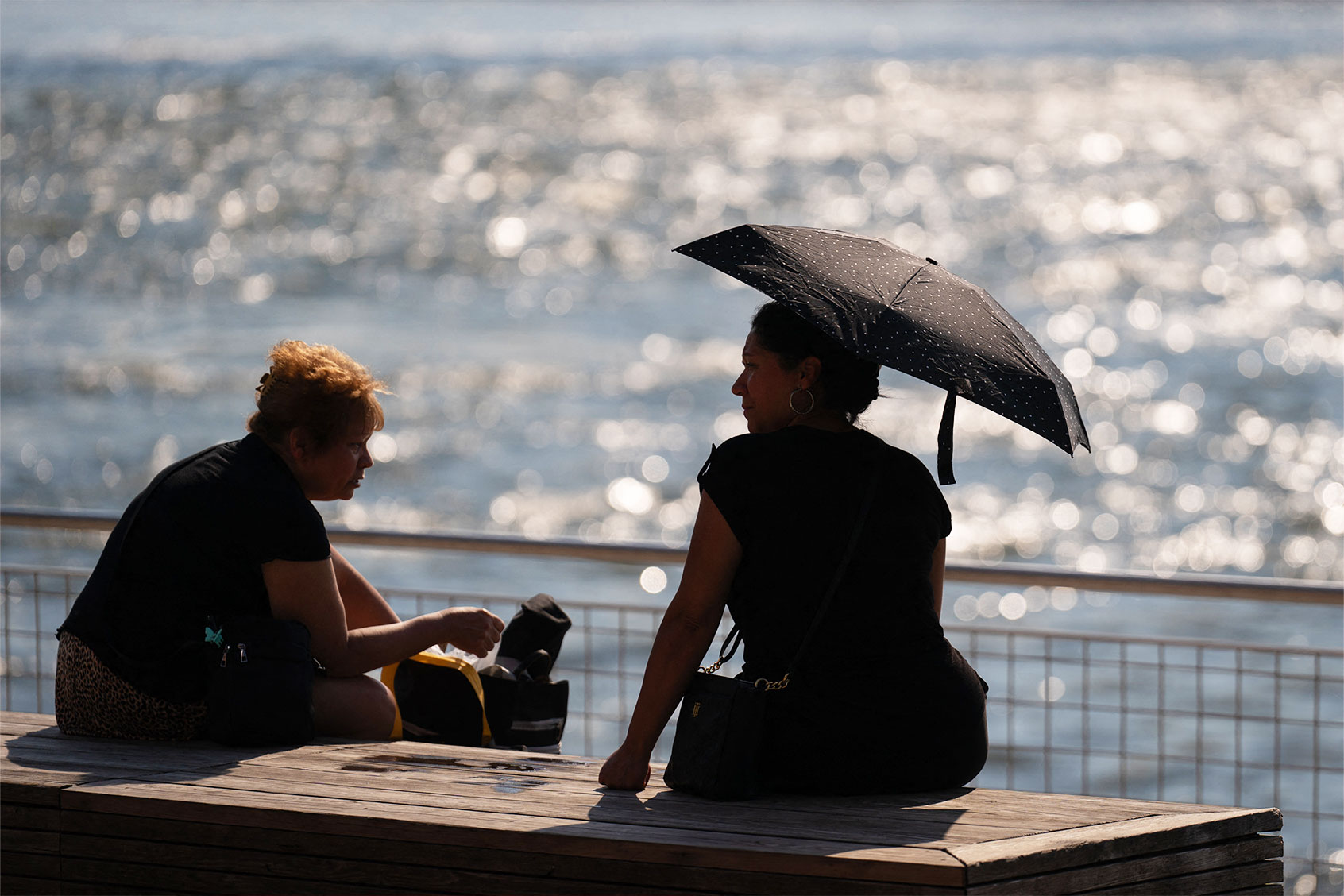A person shields themself from the sun with an umbrella as people visit Domino Park in Brooklyn, New York, as a heat wave hits the northeast US on June 18, 2024. (ADAM GRAY/AFP via Getty Images)