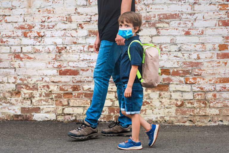 Father holding his son hand walking him back to school, boy is wearing protective face mask and carry a backpack in his shoulders. (Getty Images/Juanmonino)