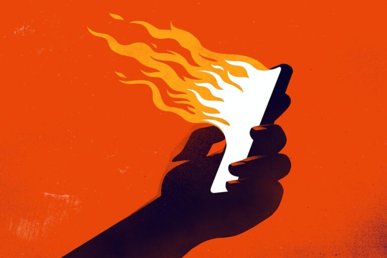 A hand holding a smartphone emanating flames. (rob dobi / Getty Images)