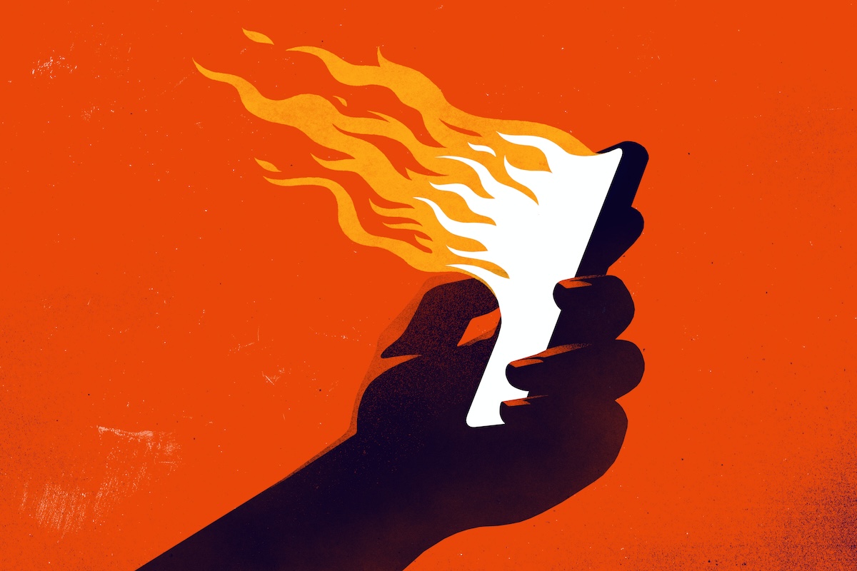 A hand holding a smartphone emanating flames. (rob dobi / Getty Images)