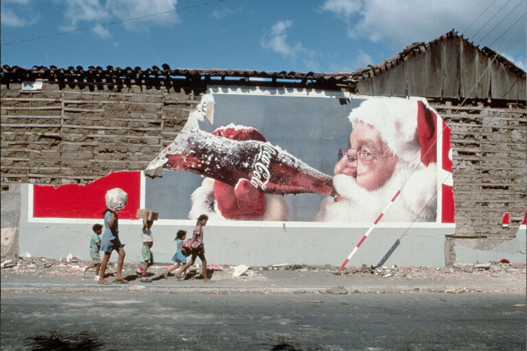 Clad in shorts and T-shirts to stay cool, residents of the capital city of Managua pick their way through the rubble beneath a billboard depicting Santa Claus drinking Coca-Cola, in Nicaragua. (Getty Images/Carl & Ann Purcell)