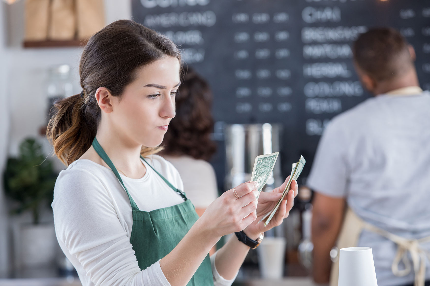 Young female barista has a disappointed expression on her face as she counts her tips at the end of the day. (Getty Images/SDI Productions)