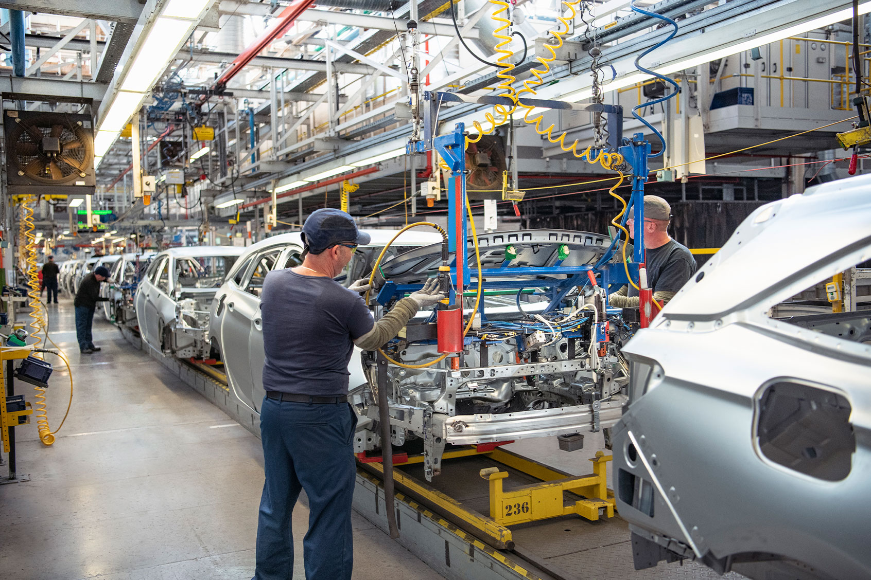 Car workers fitting bonnets to cars on production line in car factory (Getty Images/Monty Rakusen)