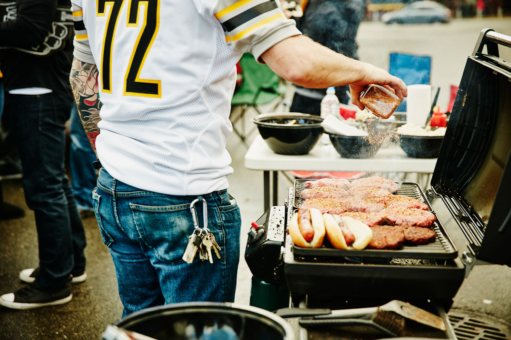 Man seasoning burgers on grill at tailgating party (Getty Images/Thomas Barwick)