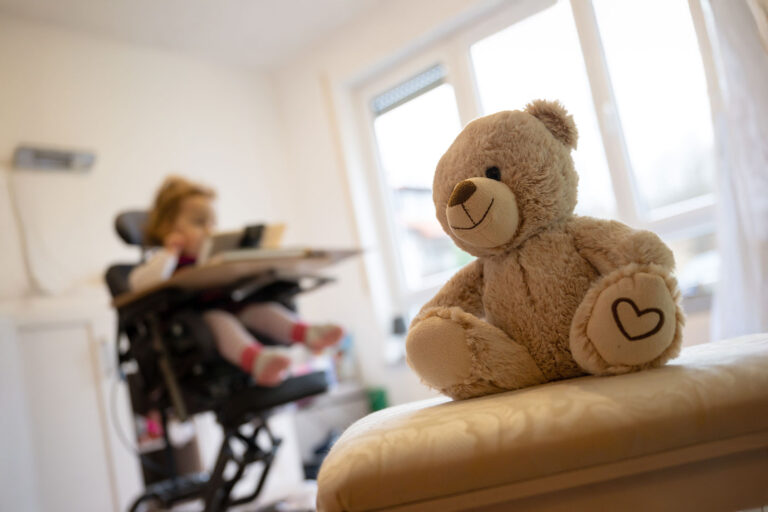 A teddy bear sits in a therapy chair in front of a child suffering from spinal muscular atrophy (SMA). (Sebastian Gollnow/picture alliance via Getty Images)