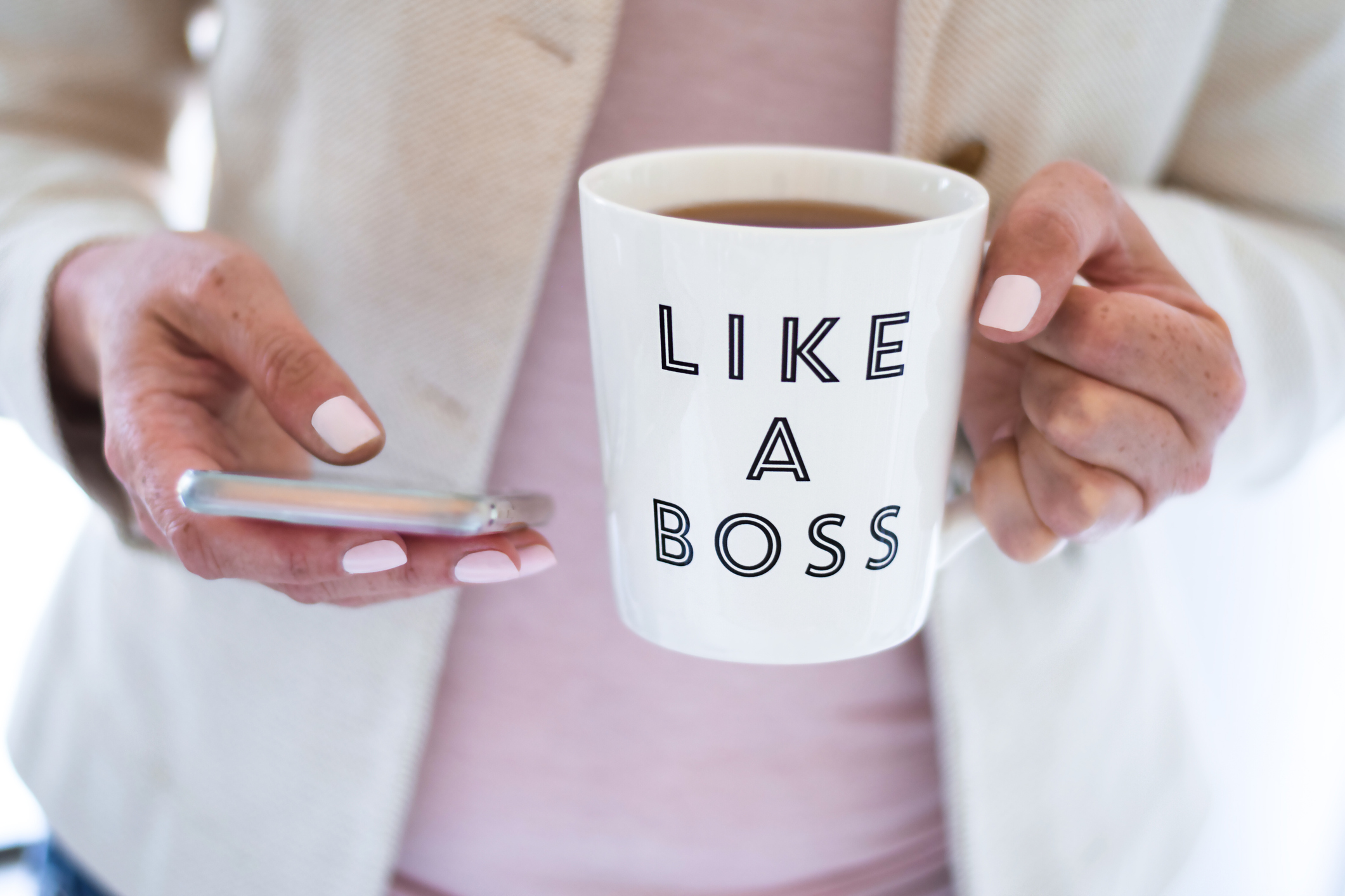 Business woman using mobile phone and holding cup (Getty Images/JulieAlexK)
