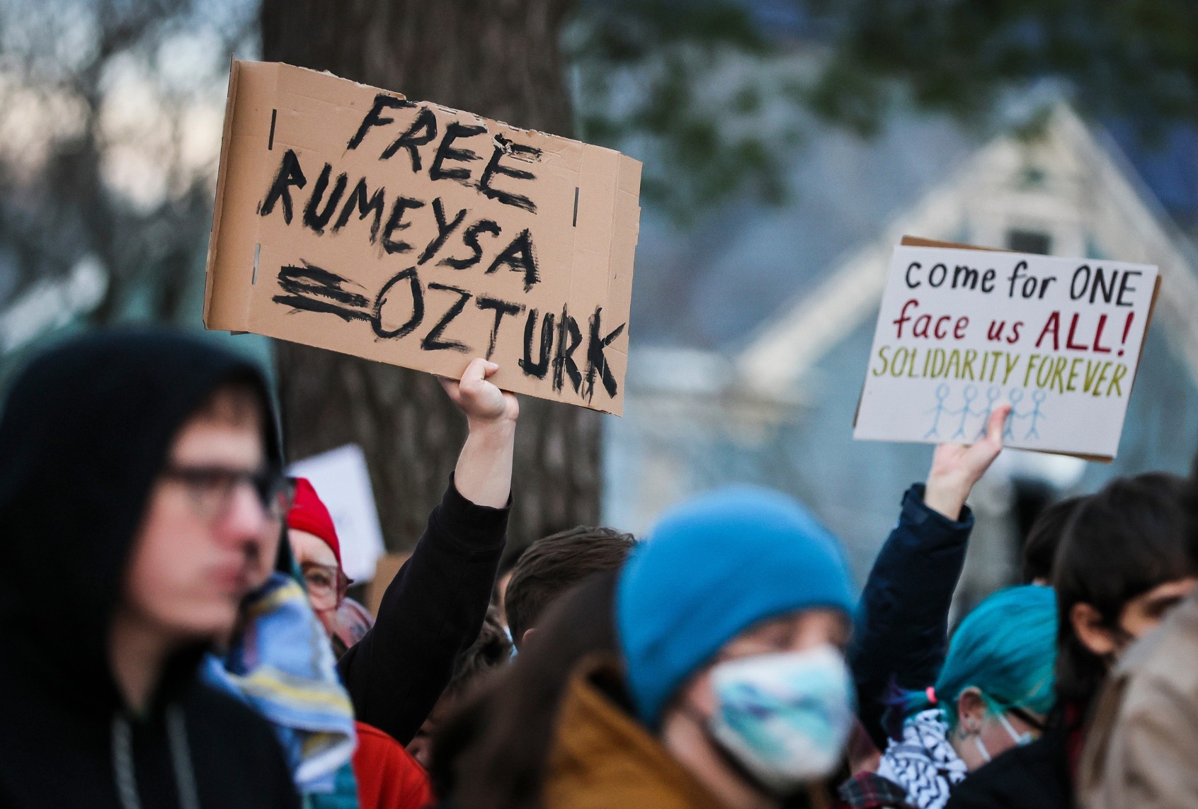 Protesters hold signs reading "Free Rumeysa Ozturk" and "come for one face us all! solidarity forever" during a demonstration at Powder House Park in Somerville, Massachusetts. = (Erin Clark/The Boston Globe via Getty Images)