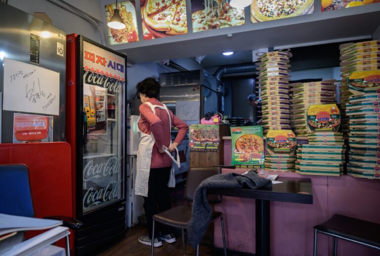 A singed message written by director Bong Joon-ho is displayed (L) as pizza restaurant owner Eom Hang-ki, 65, works in her restaurant Sky Pizza in Seoul, the inspiration for "Pizza Generation" in the film "Parasite." (ED JONES/AFP via Getty Images)