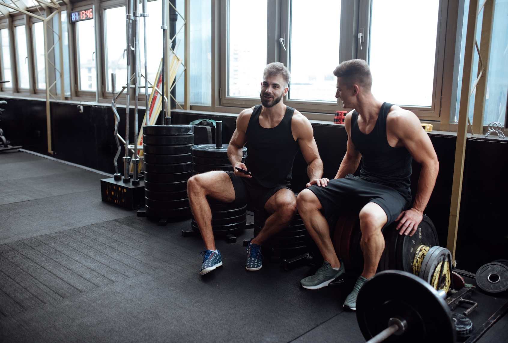 Two friends chatting and looking at phone in a gym. (Anchiy / Getty Images)