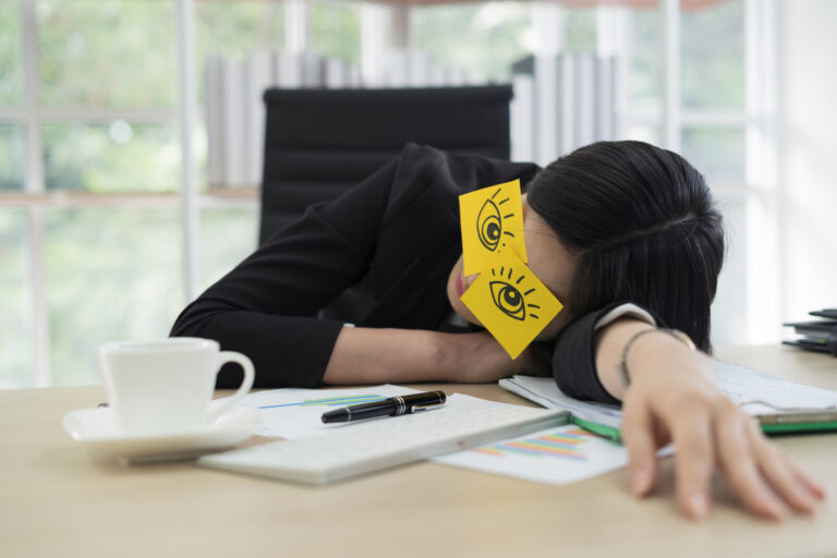 Young business woman with fake eyes painted on adhesive note sleeping at workplace in office (Getty Images/thianchai sitthikongsak)