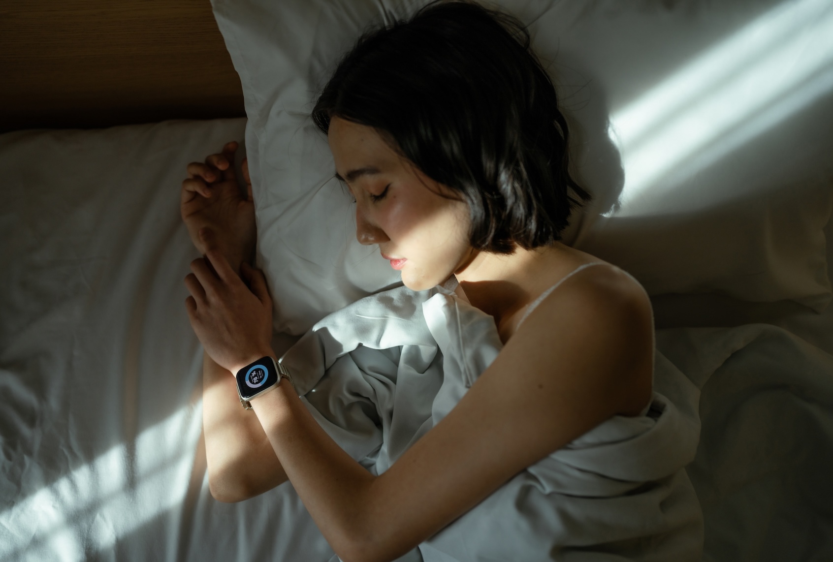 Woman sleeping peacefully in bed, wearing a smart watch to track her sleep patterns. (Getty Images / whitebalance.space)