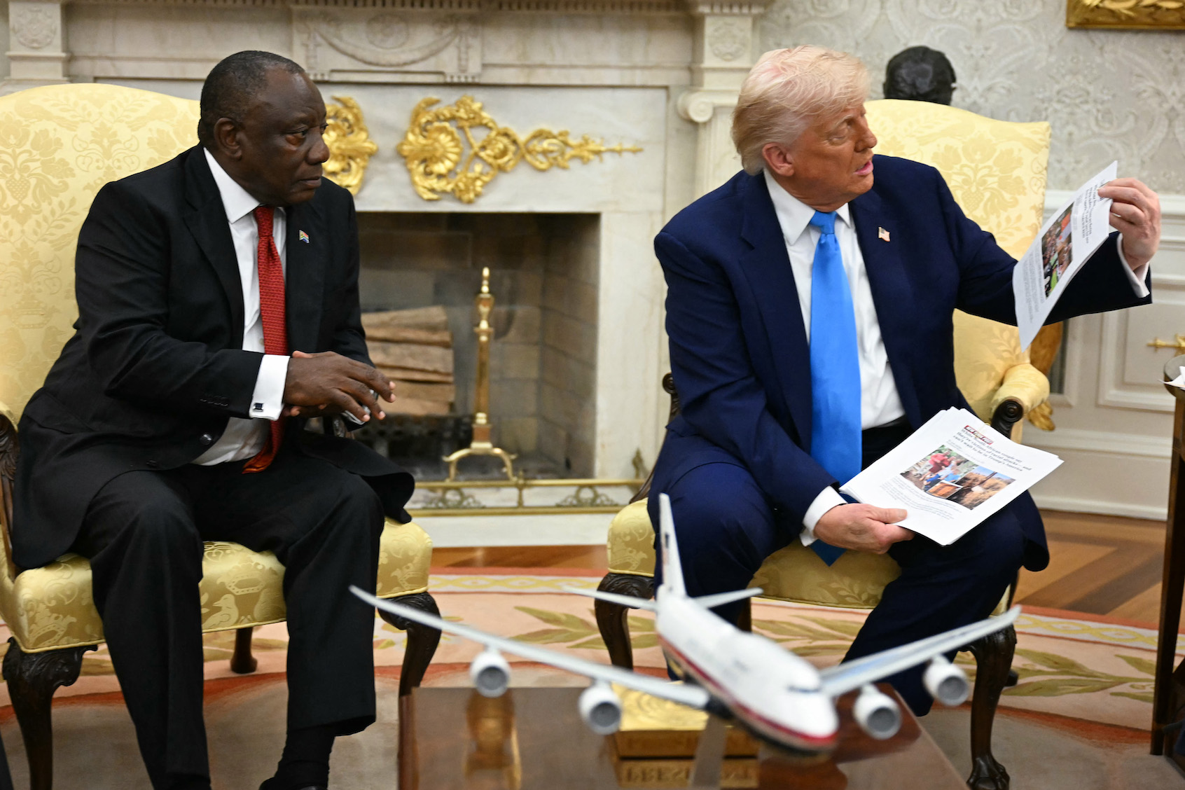 US President Donald Trump shows pictures and articles as he meets with South African President Cyril Ramaphosa in the Oval Office of the White House in Washington, DC, on May 21, 2025. South African President Cyril Ramaphosa meets Donald Trump on Wednesday amid tensions over Washington's resettlement of white Afrikaners that the US president claims are the victims of "genocide." (Photo by Jim Watson/Getty Images)