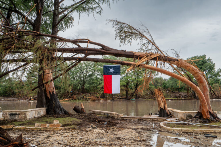 A Texas flag hangs from a storm-damaged tree on the banks of the Guadalupe River on July 13, 2025 in Center Point, Texas. (Photo by Brandon Bell/Getty Images)