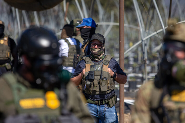 A US Immigration and Customs Enforcement agent watches as Customs and Border Protection officers hold the line against protestors who responded to a Federal Immigration raid at Glass House Farms in Camarillo, California.