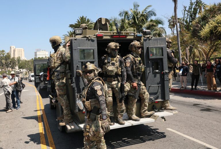 Federal agents with US Customs and Border Patrol (CBP) ride on an armored vehicle driving slowly down Wilshire Boulevard near MacArthur Park in Los Angeles, California, on July 7, 2025. (PATRICK T. FALLON/AFP via Getty Images)