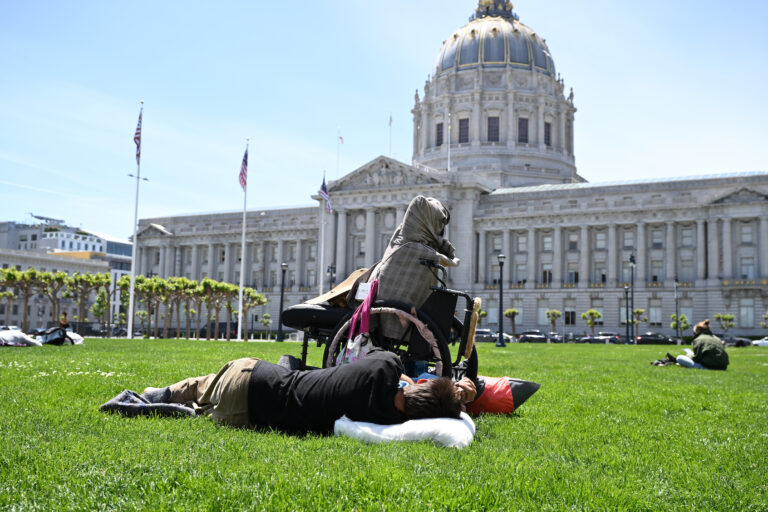 A homeless man sleeps on grass outside of the City Hall in San Francisco, California. (Photo by Tayfun Coskun/Anadolu via Getty Images)