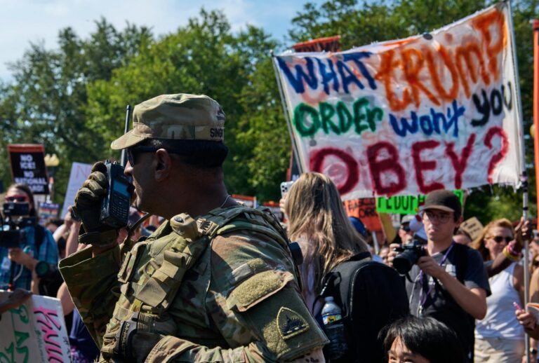 National Guardsmen are surrounded by thousands of protesters in Washington, D.C., on August 16, 2025. (DOMINIC GWINN/Middle East Images/AFP via Getty Images)