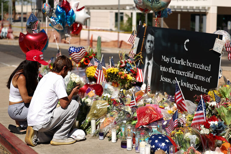 People gather before Turning Point USA headquarters in Arizona to pay tributes to Charlie Kirk. Early unverified reports claimed transgender ideation, but major outlets have since walked back their statements upon official clarification. (CHARLY TRIBALLEAU / Getty Images)