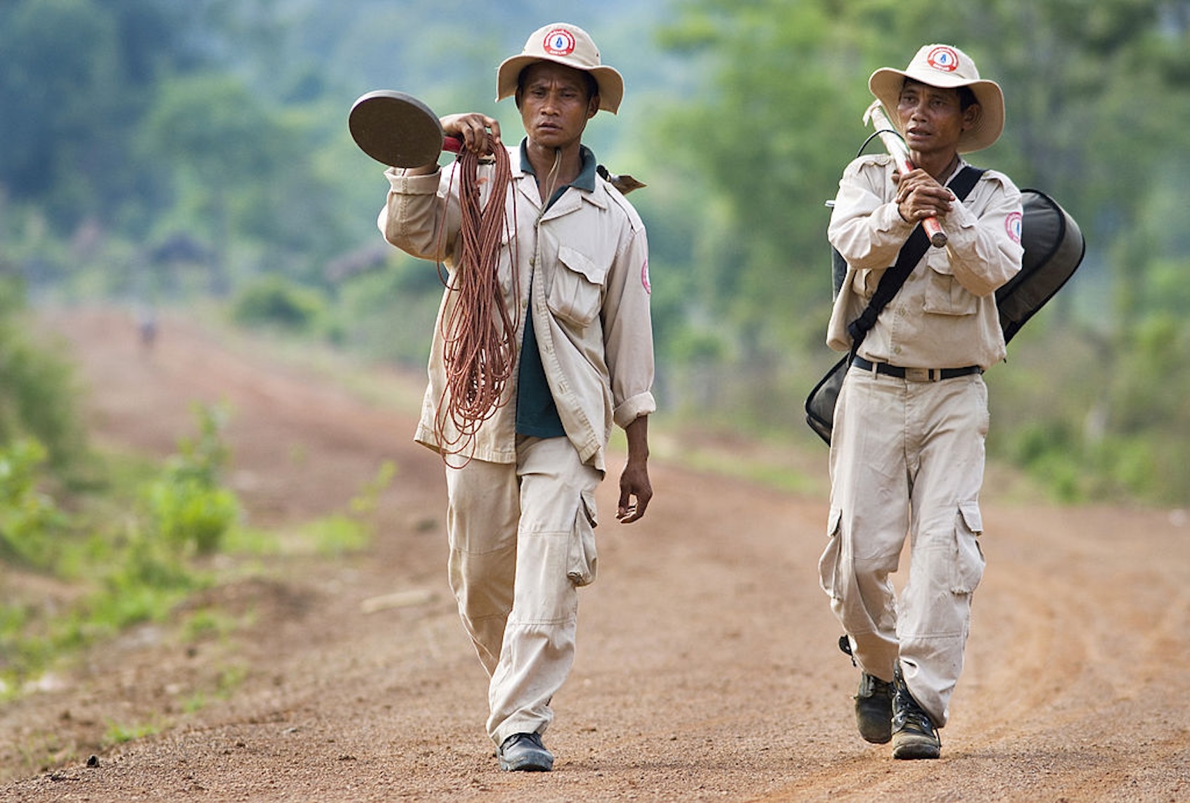 A pair of UXOLao technicians walk down a new road built atop the old Ho Chi Minh Trail. 

After spending the day finding buried explosives, A pair of UXOLao technicians walk down a new road built atop the old Ho Chi Minh Trail in Phu Vong, Attapeu, Laos. (Jerry Redfern/LightRocket via Getty Images)