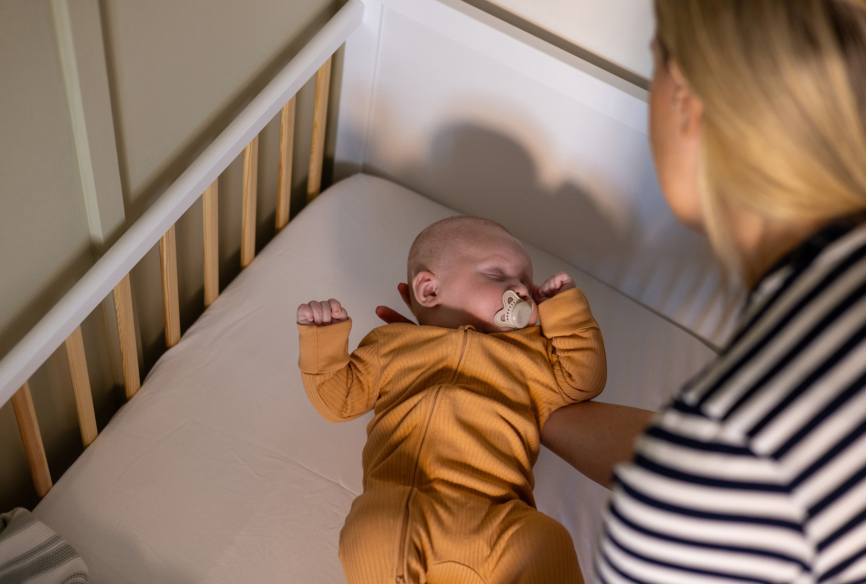 A mother places her sleeping newborn in the crib (Getty / SolStock)