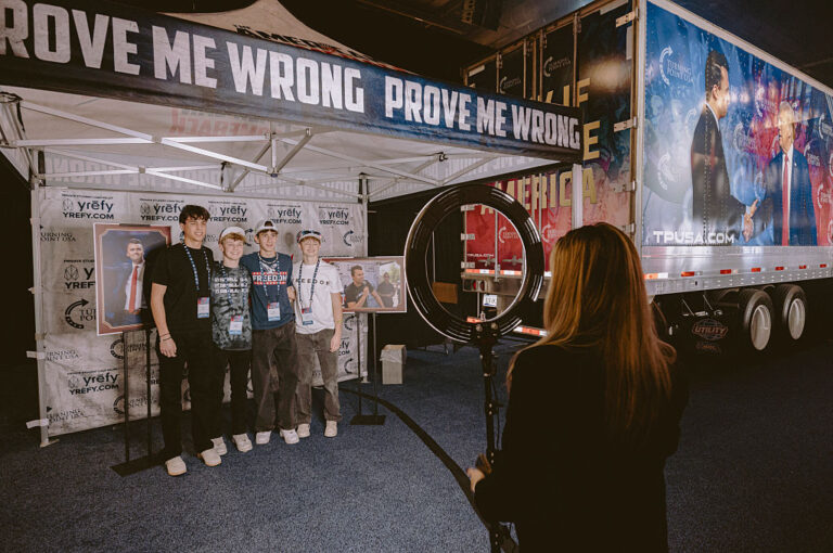 AmericaFest Conference attendees pose for pictures in a replica of the tent of Charlie Kirk's assassination location. One of the many sights, merch and other spectacles at the event. (Olivier Touron / AFP via Getty Images)