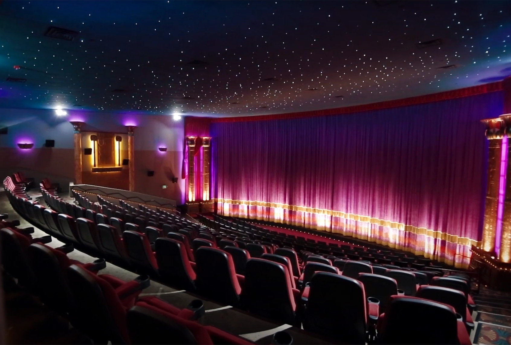 The interior of The Grand’s Pharaoh’s Theater, featuring rows of seats facing a stage framed by purple curtains and a ceiling lit like a night sky.