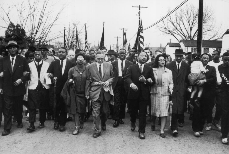 March 1965:  American civil rights campaigner Martin Luther King (1929  - 1968) and his wife Coretta Scott King lead a black voting rights march from Selma, Alabama, to the state capital in Montgomery;  among those pictured are, front row, politician and civil rights activist John Lewis (1940 – 2020), Reverend Ralph Abernathy (1926 - 1990), Ruth Harris Bunche (1906 - 1988), Nobel Prize-winning political scientist and diplomat Ralph Bunche (1904 - 1971), activist Hosea Williams (1926 – 2000 right carrying child). (Photo by William Lovelace/Daily Express/Hulton Archive/Getty Images)