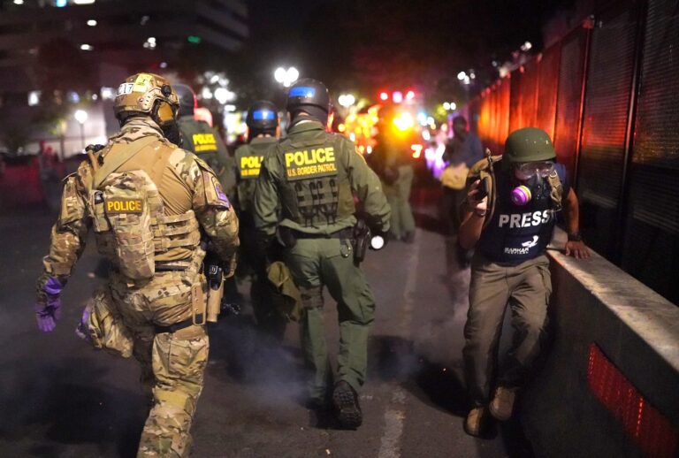 PORTLAND, OR - JULY 30: A journalist runs past federal officers after he was caught behind a police line during a protest against racial injustice and police brutality in front of the Mark O. Hatfield U.S. Courthouse in the early hours of July 30, 2020 in Portland, Oregon. Protests against the federal presence in Portland continued Wednesday following an announcement by Governor Kate Brown that federal officers would begin a phased withdrawal from the city. (Photo by Nathan Howard/Getty Images)