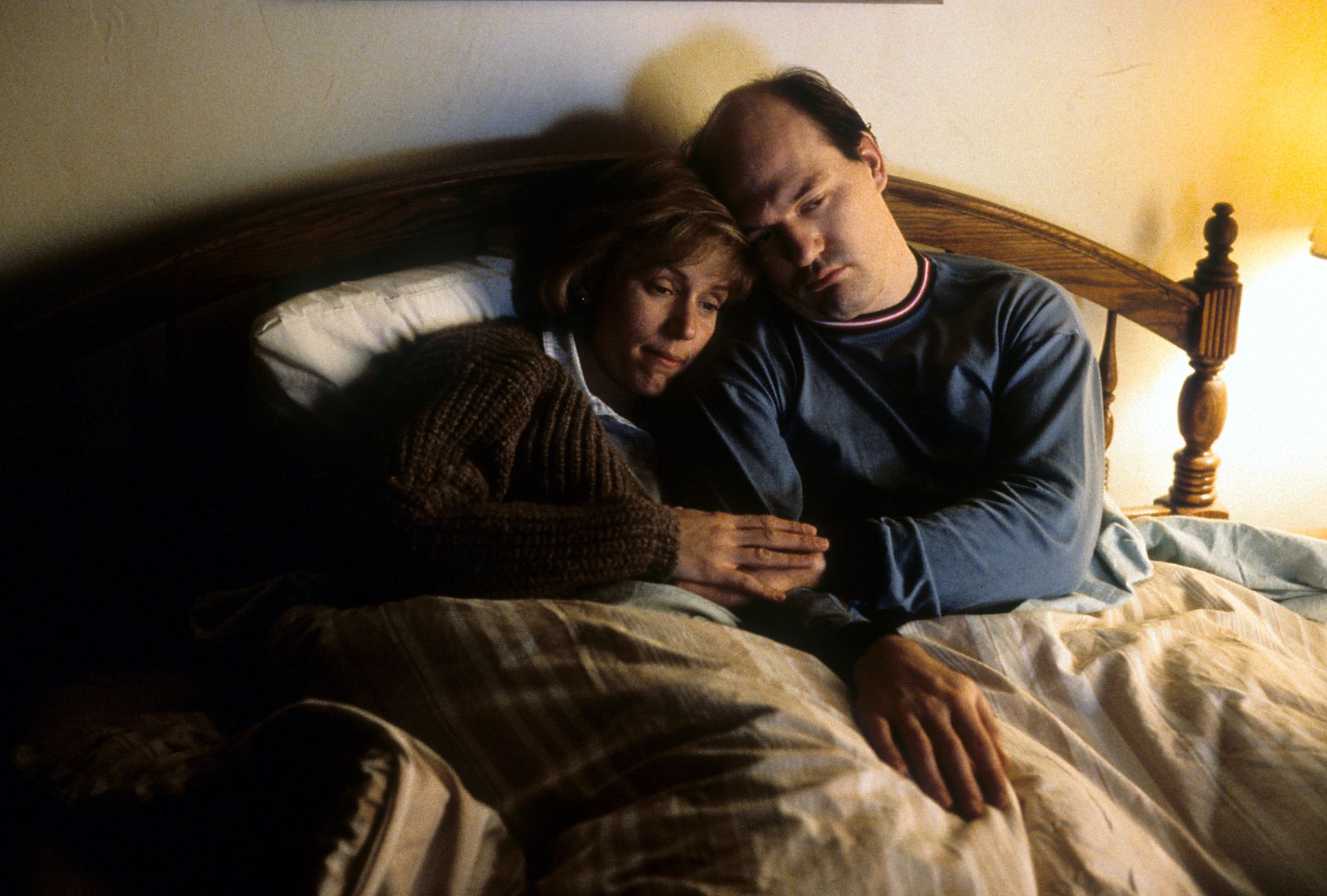A man and woman seeking comfort lean on each other in bed. Her head is on his shoulder