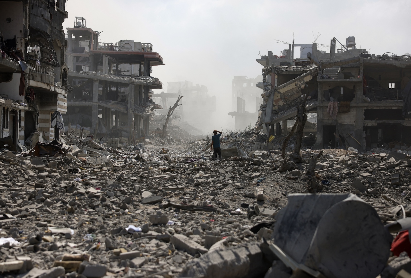 A Palestinian youth stands on a street strewn with rubble following an explosion in the Saftawi neighbourhood, west of Jabalia in the northern Gaza Strip on August 25, 2025. (Photo by BASHAR TALEB / AFP via Getty Images)