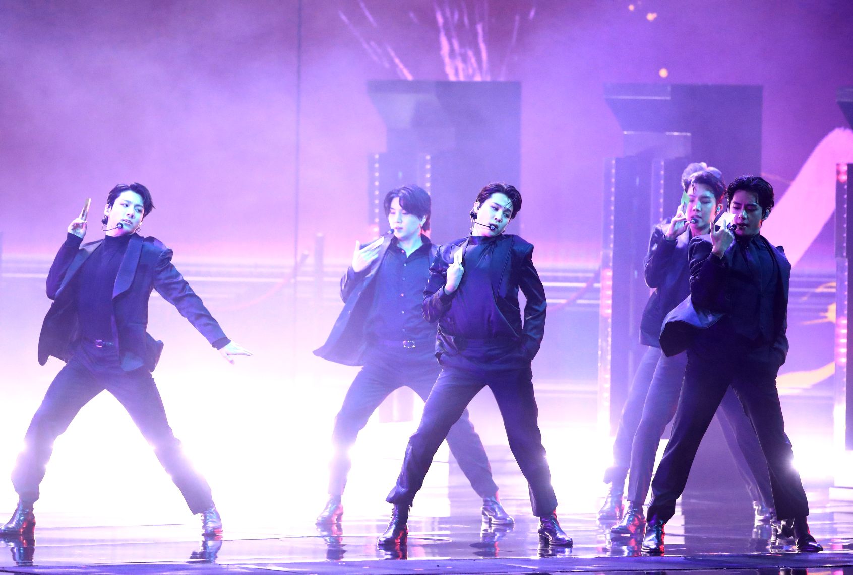 Seven men lit in a purplish hue, strike a pose in unison on stage