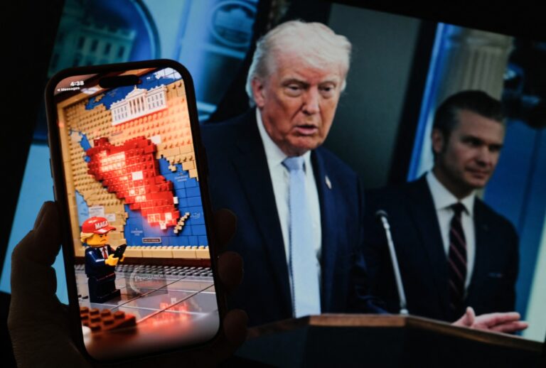 A Lego-style AI-generated war-themed video playing on a smartphone screen in front of a photo of President Donald Trump and Secretary Of Defense Pete Hegseth (Chris DELMAS / AFP via Getty Images)