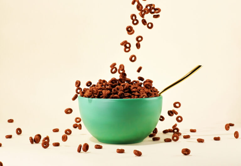 Chocolate cereal pouring into green bowl with spoon on cream background (Juj Winn / Getty Images)