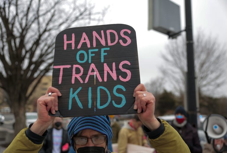 Protesters with Gender Liberation Movement and ACT UP block the entrance to the Department of Health and Human Services while protesting the Trump administration’s plan to cut federal funding to clinics providing care for transgender youth on February 17, 2026 in Washington, DC. 24 demonstrators were arrested while protesting on the final day of public comment over proposed rules that critics say would effectively ban gender-affirming care for transgender youth nationally. (Photo by Heather Diehl/Getty Images)