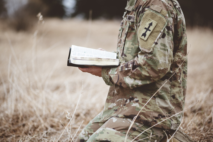 A soldier reads Holy Scripture in a field. The military is consolidating faiths to streamline its chaplaincy services. (Wirestock / Getty Images)
