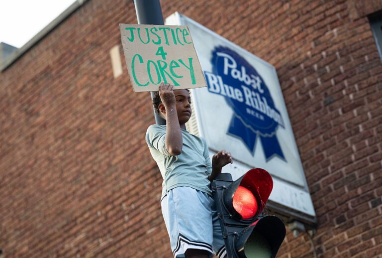 A protester holds a sign at the intersection where Corey Ruiz was shot and killed police on July 23, 2026 in Madison, Wisconsin. (Scott Olson/Getty Images)