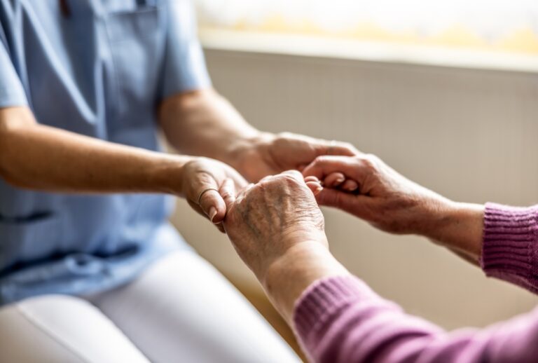 A nurse holding the hand of an elderly person. (SimpleImages via Getty Images)