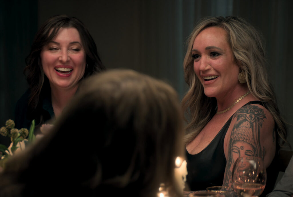Two women laugh while seated at a candlelit dinner table.